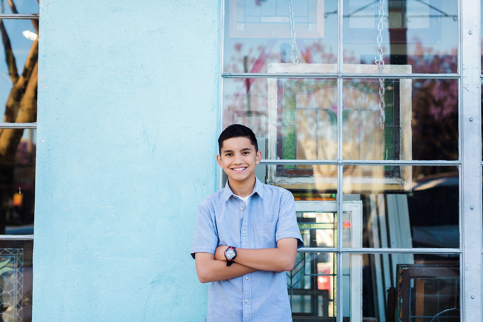 14 years old boy posing in front of a store. Little Italy, blue wall. Urban photo shoot. Graduation photo.