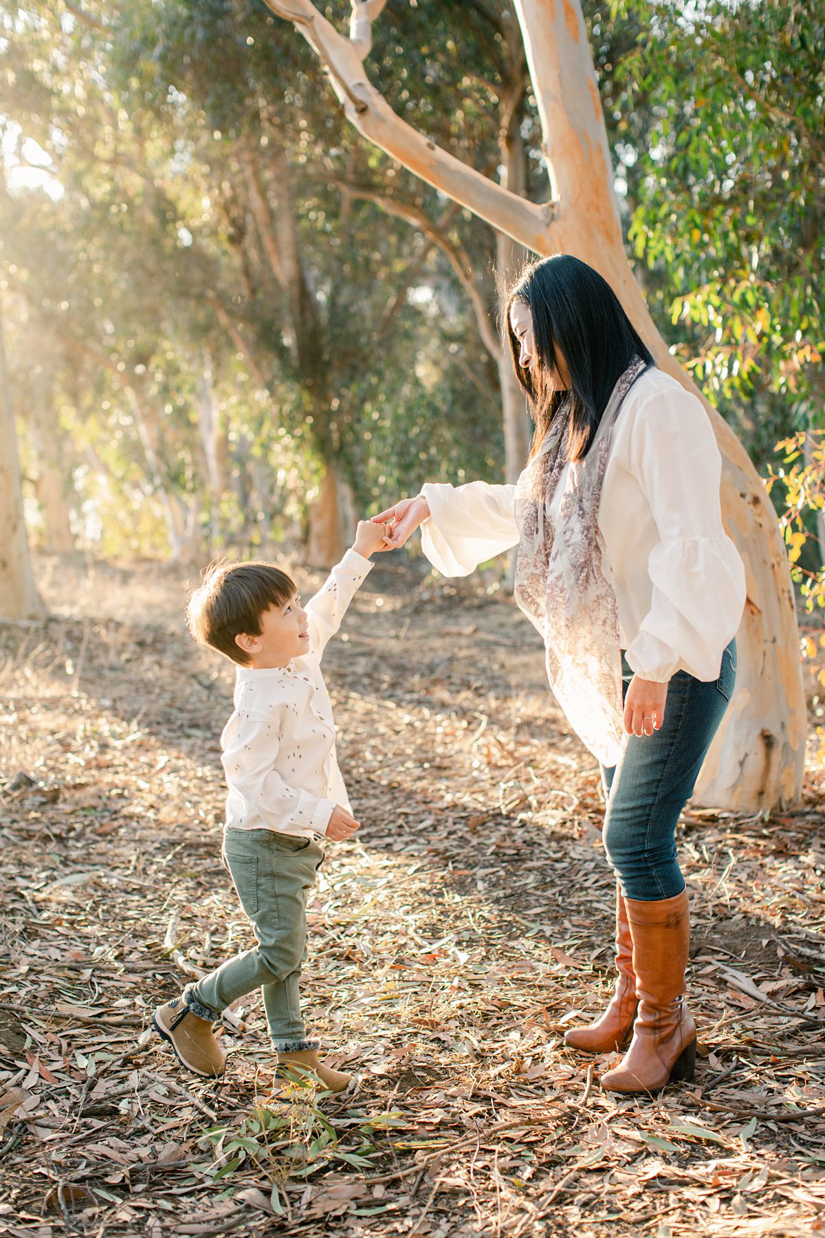 a mom and son dancing wearing white shirt in the forest. Sunset golden hour.