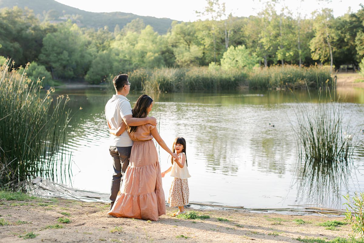 a family standing in front of a pond. A girl is looking back at the camera.