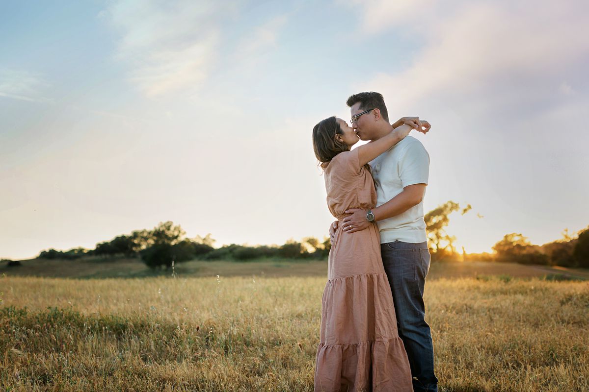 A couple holding each other and kissing in open field. sunset.