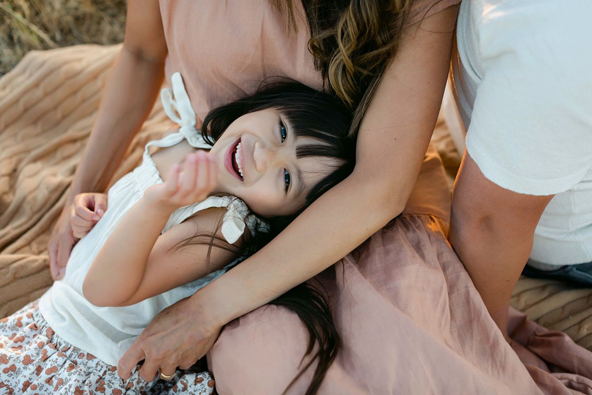 a girl laying on mom'd lap, looking up at the camera, laughing.